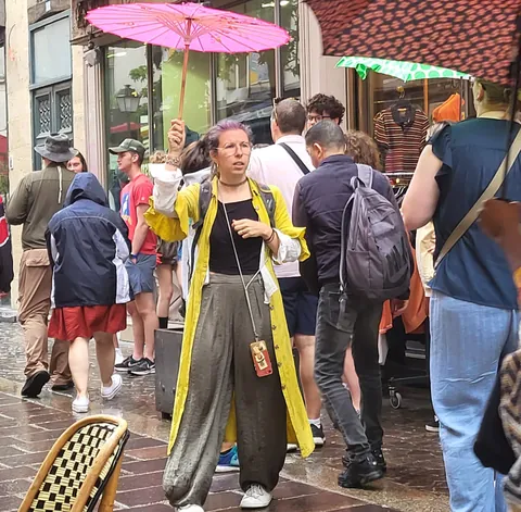Une femme en ciré jaune sous une ombrelle rose au milieu d’une foule