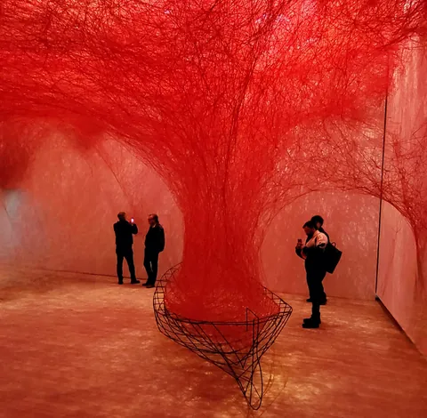 Une installation de fils rouges dans une salle, deux visiteurs