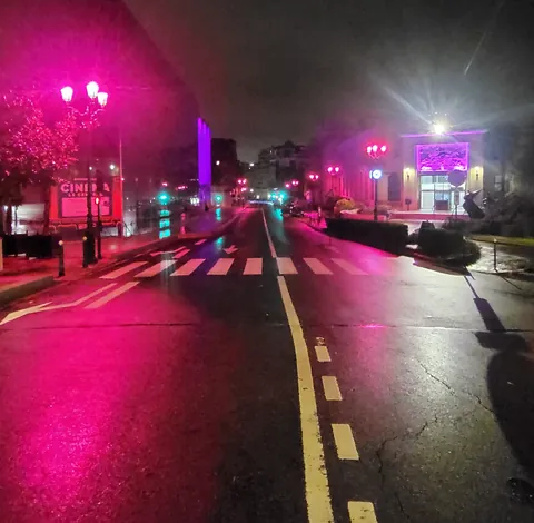 Une avenue la nuit, baignée de lumière rose par les réverbères