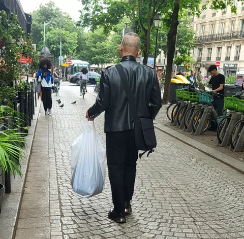 Un homme en cuir noir avec un sac plastique, de dos