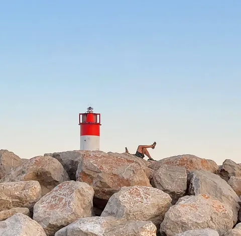 Un homme allongé sur les rochers d’une jetée, au pied d’un phare