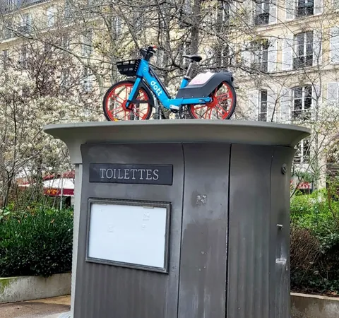 Un vélo en libre-service bleu et rouge posé sur le toit d’une sanisette