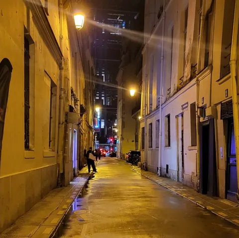 Une rue étroite la nuit, éclairée par des réverbères, un passant au loin