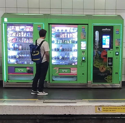 Un homme sac au dos devant des distributeurs de friandises verts, sur un quai de métro