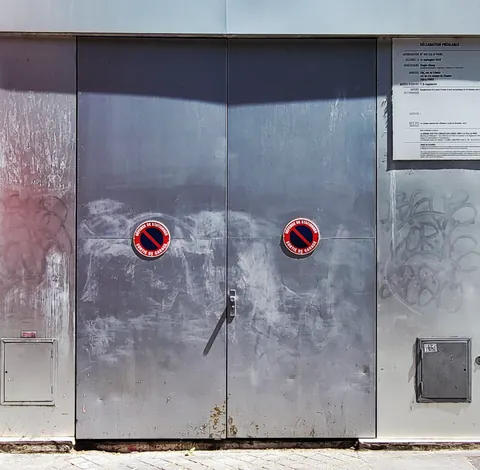 Une porte métallique dont les deux hublots rouges font comme des yeux