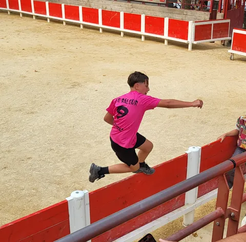 Un garçon en t-shirt rose qui saute la barrière d’une arène