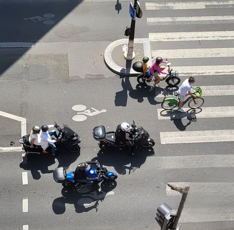 Deux motos et des cyclistes dans un carrefour, vus d’en haut