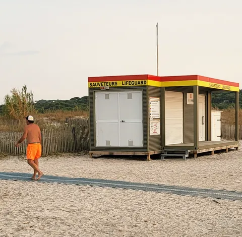 Un poste de sauveteurs fermé sur une plage, un passant en short orange