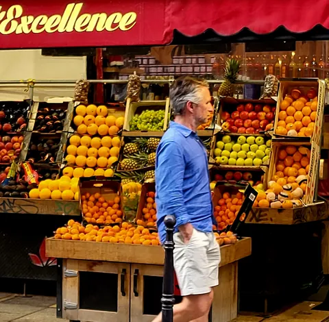 Un homme en chemise bleue devant un étal de fruits « Excellence »