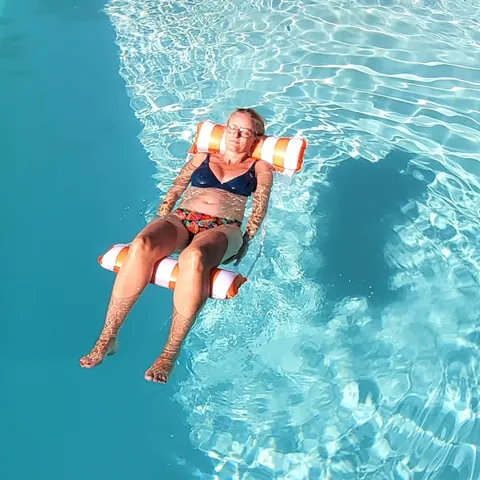 Une femme qui flotte sur une bouée-fauteuil dans une piscine turquoise, vue d’en haut
