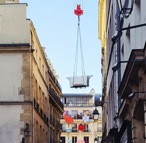Une baignoire suspendue à une grue au-dessus d’une rue étroite