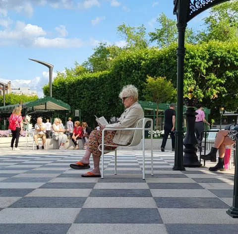 Une vieille dame qui lit sur un sol en damier, dans un parc