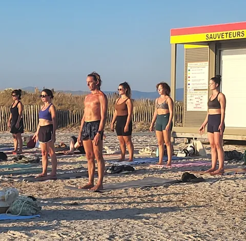 Des gens en ligne qui font du yoga sur la plage devant un poste de sauveteurs