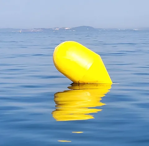 Une grosse bouée jaune qui se reflète dans une mer calme