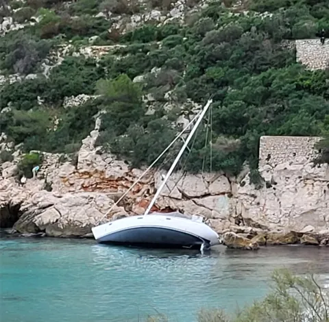 Un voilier échoué, couché sur les rochers d’une crique
